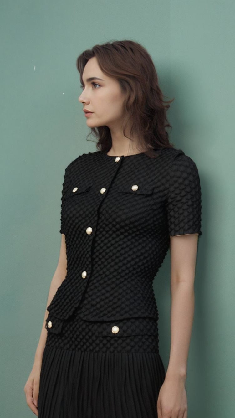 Woman wearing a black outfit with gold buttons against a green wall